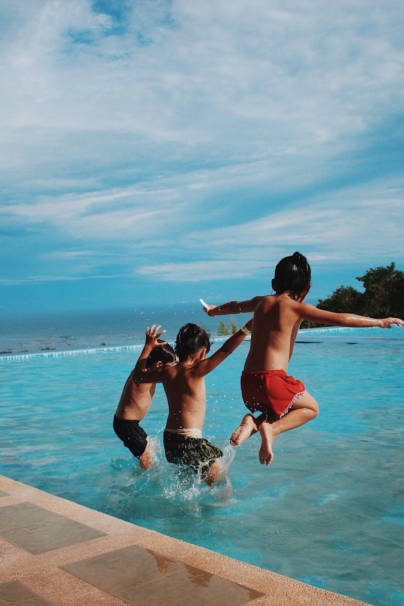 Two children joyfully jump into a pool on a sunny day, embodying excitement and summer vibes.